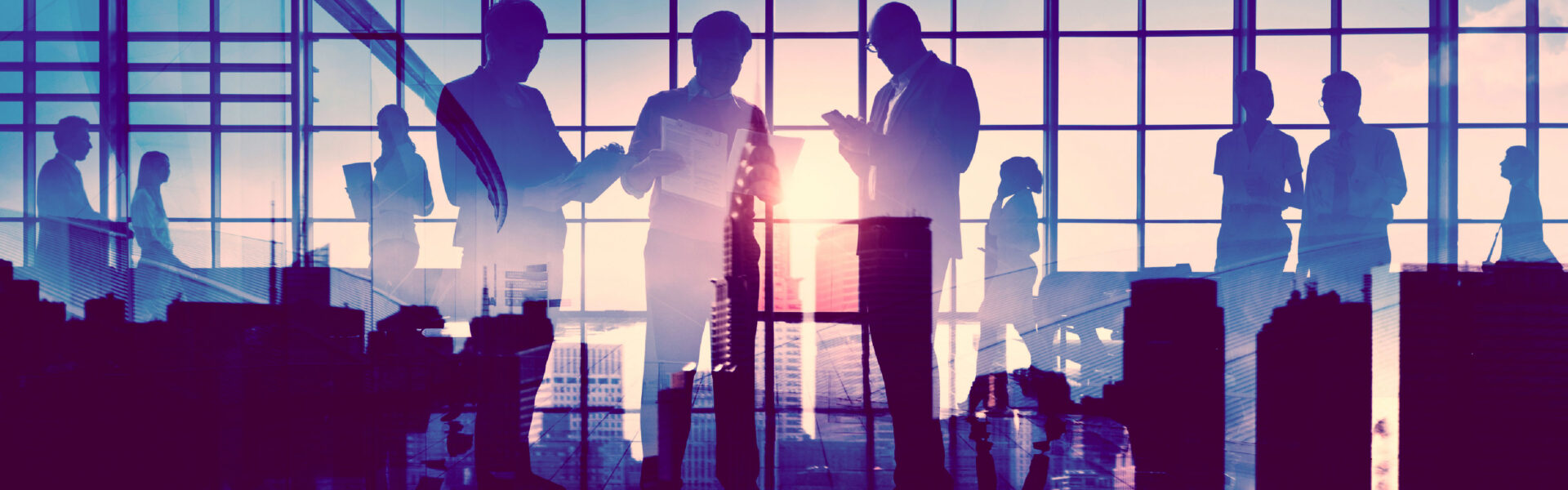 Silhouetted business professionals interact in front of a large window overlooking a city skyline at sunrise or sunset. A double exposure effect blends their figures with urban architecture, symbolising corporate collaboration and the intersection of business and city life.